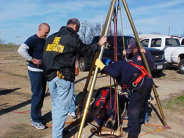 Fire fighters standing around the manhole rigging, double checking safety gear.